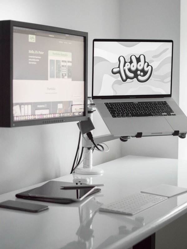 Laptop on a stand with two monitors on a desk, displaying a logo in yoodesk ultra series dual motor standing desk.